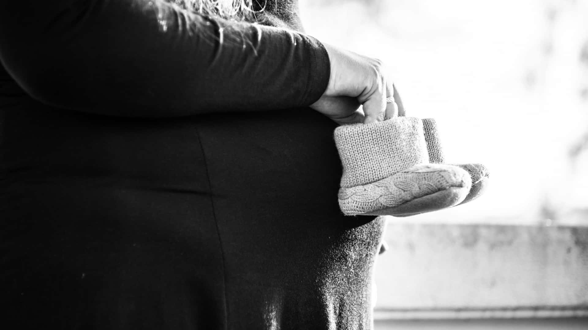 Artystyczna czarno-biała sesja ciążowa w Katowicach – zbliżenie na brzuszek przyszłej mamy trzymającej malutkie, wełniane buciki niemowlęce, nastrojowa fotografia brzuszkowa Śląsk.