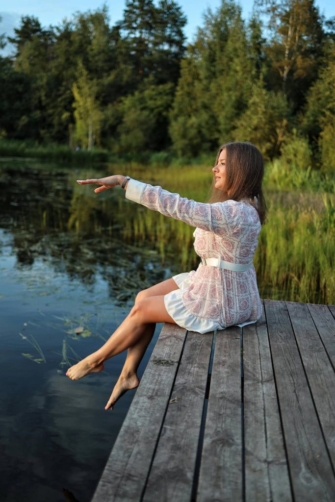 Relaksująca sesja kobieca na Śląsku – młoda kobieta w letniej sukience siedząca na drewnianym pomoście nad jeziorem, bose stopy, naturalna fotografia lifestyle Katowice.