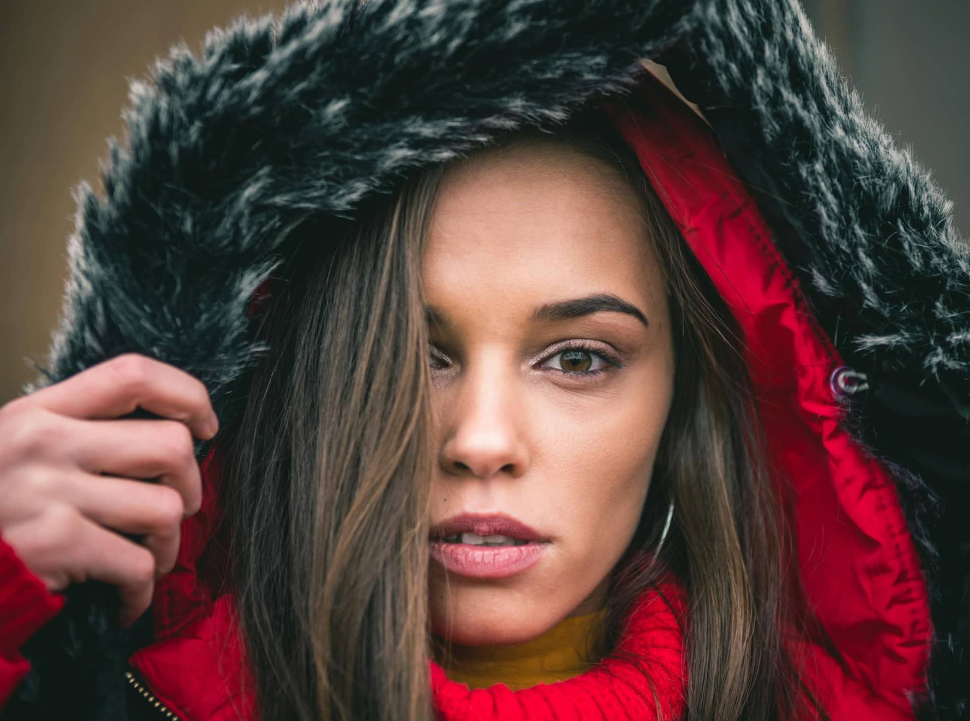 Artystyczna sesja kobieca Katowice – bliski portret pięknej kobiety w czerwonej kurtce z futrzanym kapturem, zmysłowe spojrzenie, profesjonalna fotografia portretowa Śląsk.