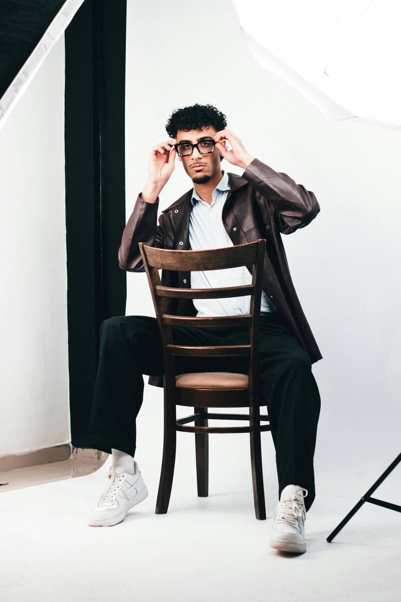 Męska sesja portretowa w studio w Katowicach – model w brązowej skórzanej kurtce i okularach siedzący tyłem na krześle, minimalistyczne tło, fotografia wizerunkowa Śląsk.