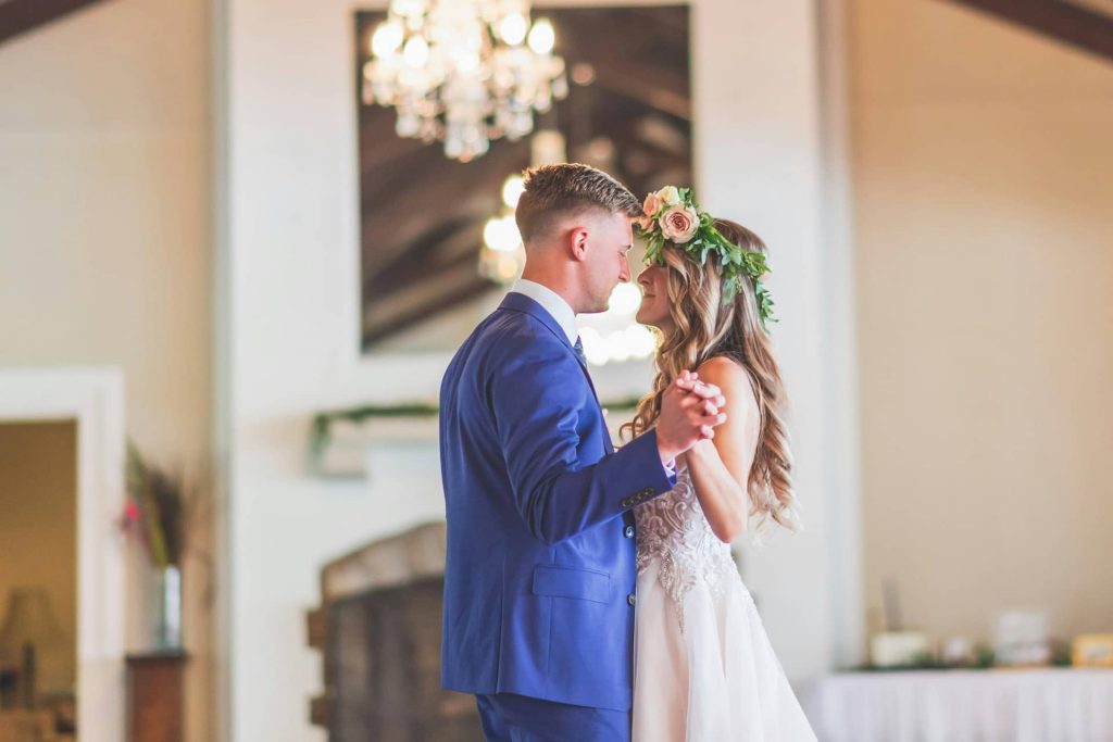 Romantyczny pierwszy taniec pary młodej w eleganckiej sali bankietowej, panna młoda w wianku z żywych kwiatów i pan młody w niebieskim garniturze, reportaż ślubny Katowice.