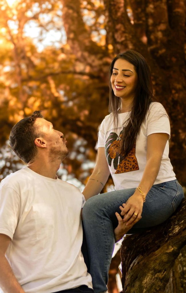 Wesoła sesja dla par Katowice – mężczyzna w białym t-shircie i kobieta w jeansach siedząca na drzewie, jesienne złote liście w tle, naturalna fotografia narzeczeńska Śląsk.