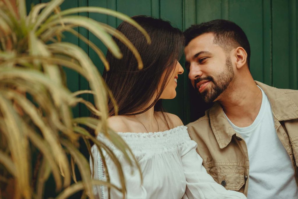 Romantyczna sesja dla par Katowice – zbliżenie na uśmiechniętą parę patrzącą sobie w oczy, lifestylowa fotografia narzeczeńska na tle zielonej ściany i roślin, Śląsk.