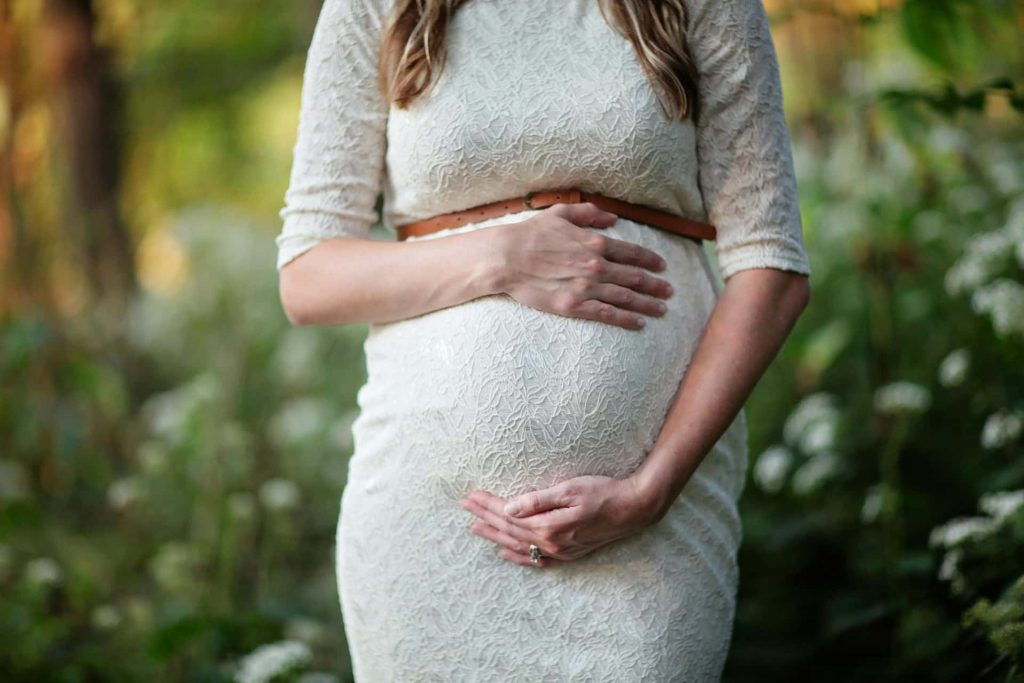 Romantyczna sesja ciążowa w plenerze Katowice – zbliżenie na dłonie przyszłej mamy na brzuszku, biała koronkowa suknia ciążowa, naturalna fotografia brzuszkowa Śląsk.