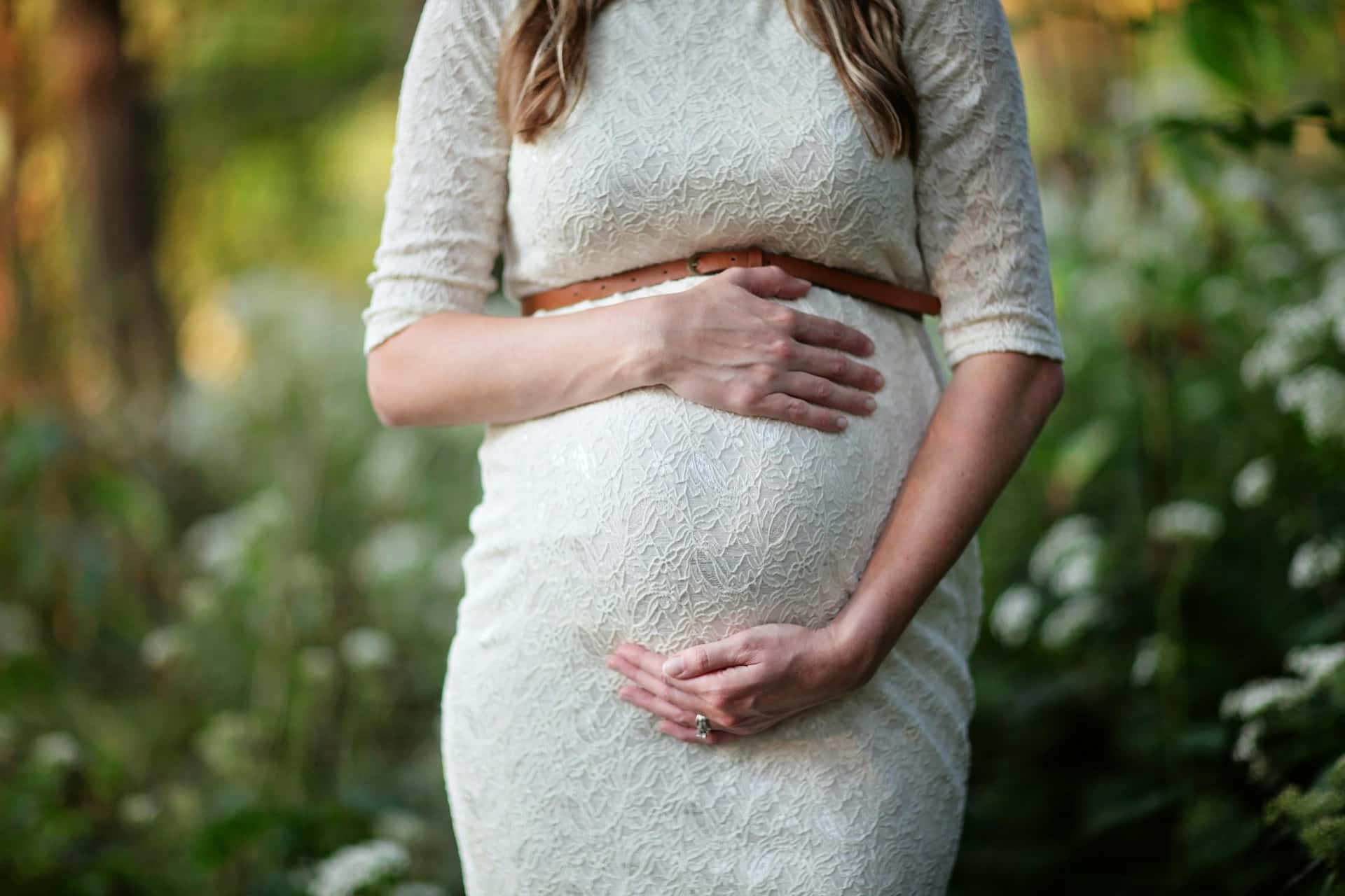 Romantyczna sesja ciążowa w plenerze Katowice – zbliżenie na dłonie przyszłej mamy na brzuszku, biała koronkowa suknia ciążowa, naturalna fotografia brzuszkowa Śląsk.