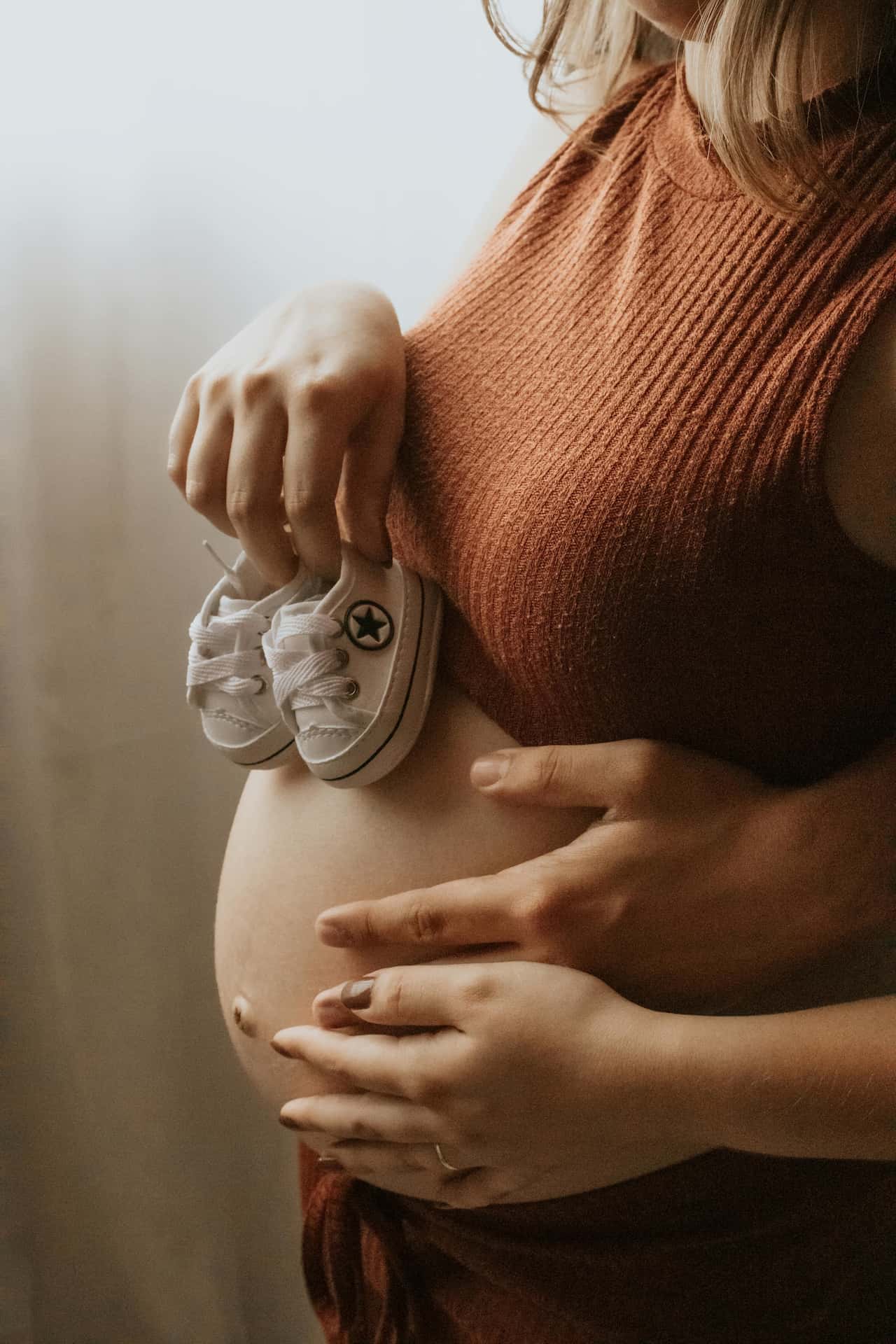 Naturalna sesja ciążowa w domu Katowice – kobieta w ciąży w ciemnym golfie patrząca przez okno, miękkie światło dzienne, fotografia brzuszkowa lifestyle Śląsk.
